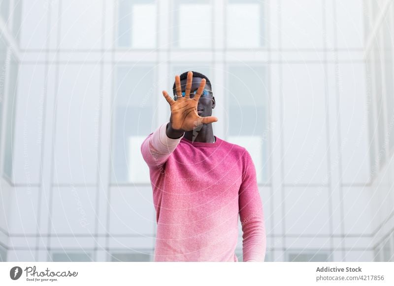 Schwarzer Mann mit verdecktem Gesicht und Stopp-Geste auf der Straße in der Stadt Deckblatt stoppen Zeichen nein Tierhaut Stil trendy verbieten gestikulieren