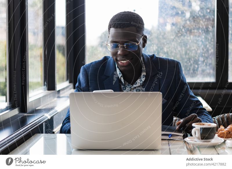 Stilvolle ethnische Führungskraft mit Smartphone und Laptop in einem Cafe Exekutive Arbeit plaudernd gut gekleidet Frühstück Mann Café benutzend Apparatur Gerät