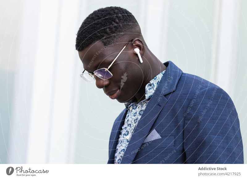 Zufriedener schwarzer Geschäftsmann, der in der Stadt mit Ohrstöpseln Musik hört zuhören Stil Großstadt Stadtzentrum gut gekleidet Unternehmer Inhalt männlich
