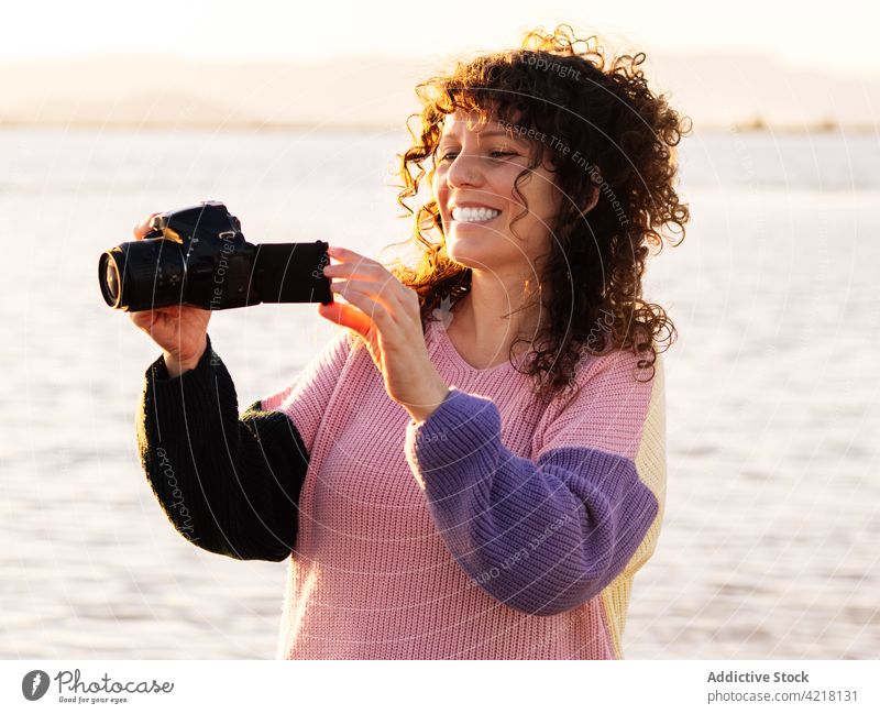 Glückliche Frau mit Fotoapparat am Strand MEER Reisender prüfen heiter Fotografie Natur Lächeln ethnisch Urlaub reisen Tourist Feiertag positiv genießen