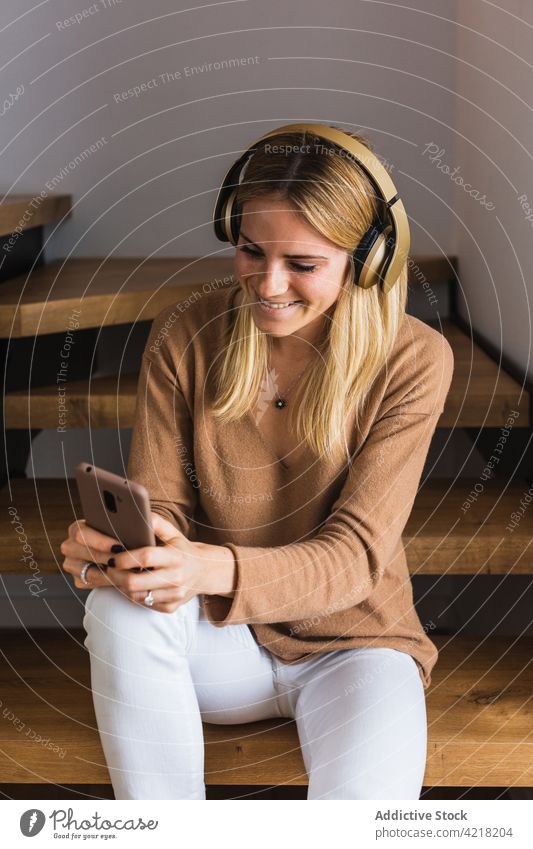 Lächelnde Frau, die zu Hause mit Kopfhörern Musik hört zuhören heimwärts Smartphone Browsen Gesang genießen benutzend Apparatur sitzen Surfen Gerät