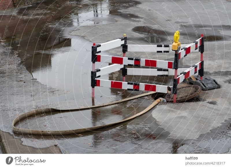 Absperrung mit Gulli und Pfütze Gullideckel Barke rot weiss Baustelle weiß Barriere Schutz Verbote rot-weiß Straßenbau Zaun Bauzaun Schlauch Überschwemmung