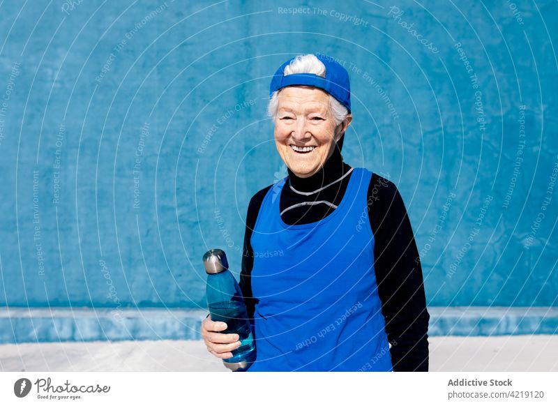 Fröhliche ältere Sportlerin mit Wasserflasche im Outdoor-Sportzentrum Zahnfarbenes Lächeln Flasche Sportkleidung Vitalität aktiv Fitness reif Motivation Energie