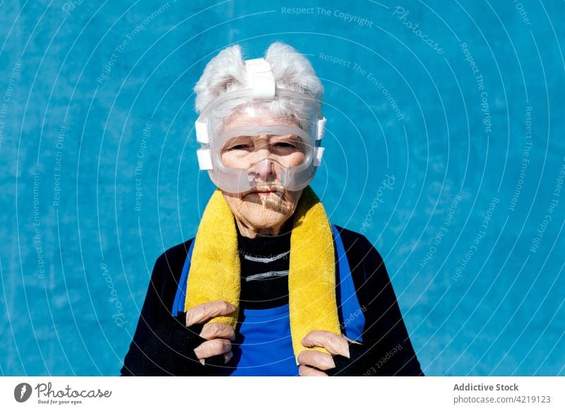 Ältere Frau mit Kopfbedeckung beim Boxen und Handtuch auf der Schulter Sportlerin Boxsport Senior Schutzhelm ernst sportlich aktiv Beschützer Energie reif