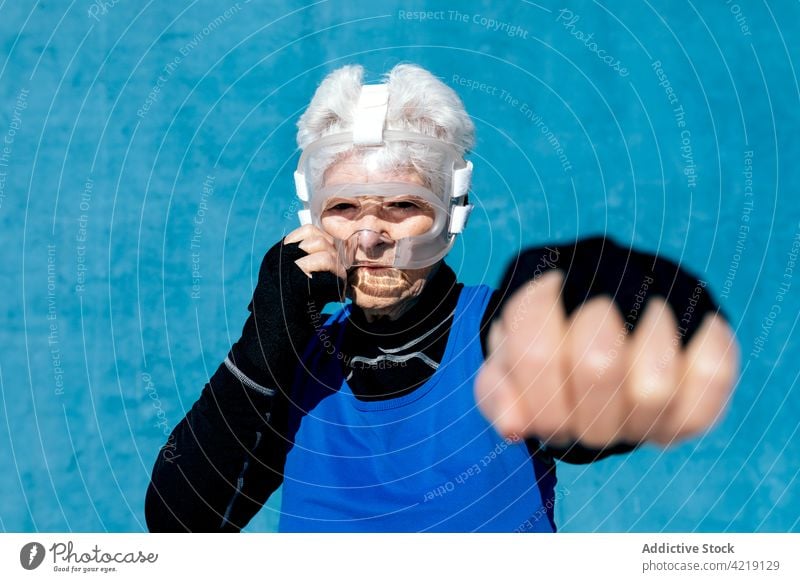 Seriöse Seniorensportlerin mit Boxer-Kopfbedeckung schlägt in die Luft Sportlerin Boxsport Bowle Training ernst sportlich aktiv schützend Schutzhelm Fokus