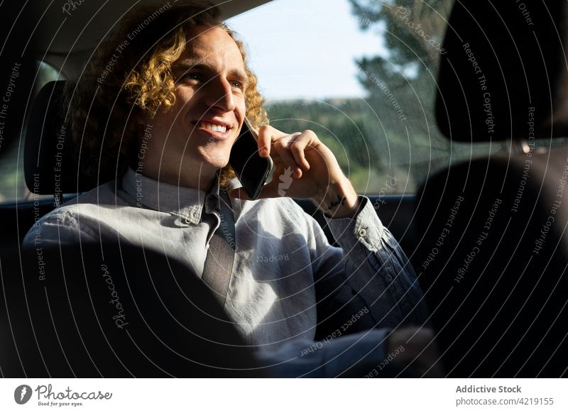 Glücklicher Mann, der im Auto mit seinem Smartphone spricht PKW Fahrer reden Lächeln Kommunizieren Natur Ausflug männlich jung heiter Lifestyle Stil Fahrzeug