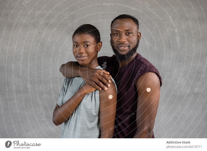 Ethnisches Paar mit Pflaster auf dem Arm nach einer Impfung Impfstoff Heftpflaster Lächeln Afroamerikaner ethnisch Frau Umarmen Glück Streifen schwarz Kur