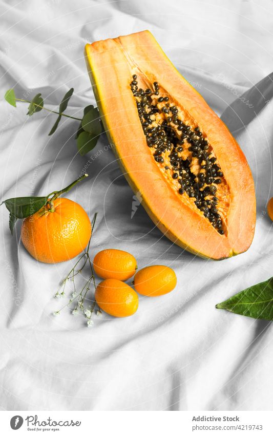 Papaya zwischen Mandarinen und Kumquats auf geknittertem Stoff schneiden Frucht tropisch natürlich frisch Vitamin Blatt Gewebe geschnitten Hälfte Samen reif
