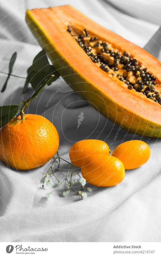 Papaya zwischen Mandarinen und Kumquats auf geknittertem Stoff schneiden Frucht tropisch natürlich frisch Vitamin Blatt Gewebe geschnitten Hälfte Samen reif