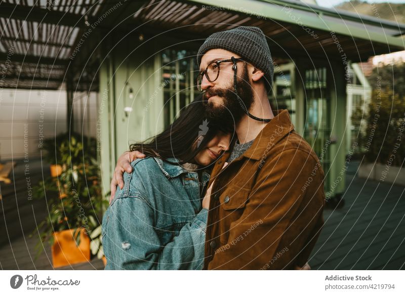 Zärtliches Paar, das sich auf einer Terrasse in der Nähe eines Holzgebäudes umarmt Umarmung Stil Hipster jung Umarmen Liebe trendy Outfit romantisch