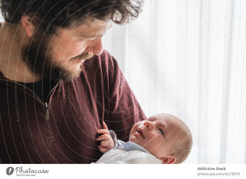 Vater umarmt gähnendes Baby in Plaid zu Hause Umarmen Vaterschaft Säuglingsalter Glück achtsam heimwärts Porträt Mann Zuneigung Papa Freude Lächeln Zusammensein
