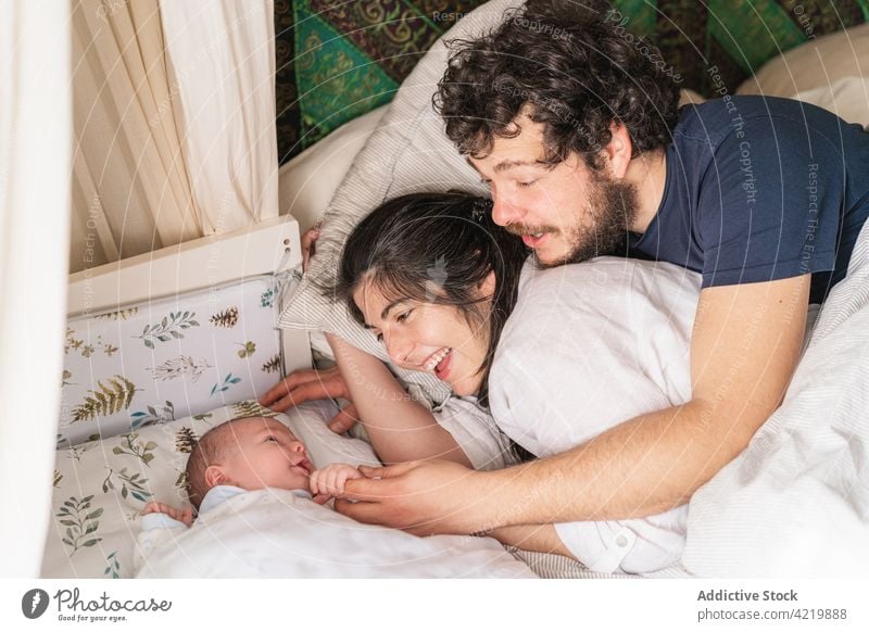Lächelnde Familie mit neugeborenem Baby, das im Bett liegt interagieren Elternschaft Säuglingsalter heiter Zeit verbringen heimwärts idyllisch Vater Mutter