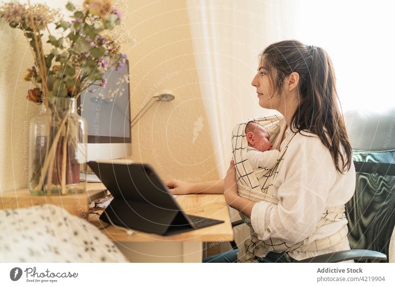 Mutter hält Baby und arbeitet am Computer zu Hause Frau freiberuflich neugeboren Mutterschaft multitask heimwärts Schreibtisch Notebook Blume Bonden schreiben