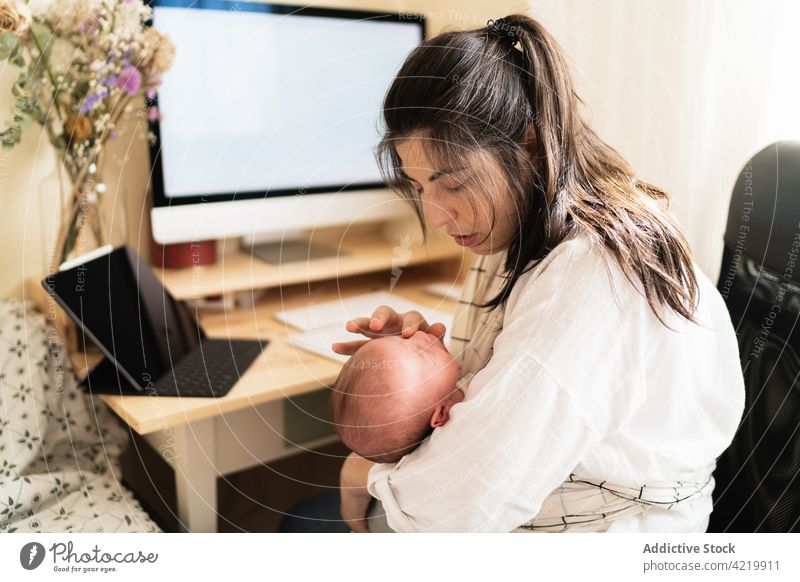 Mutter hält Baby und arbeitet am Computer zu Hause Frau freiberuflich neugeboren Mutterschaft multitask heimwärts Schreibtisch Notebook Blume Bonden schreiben