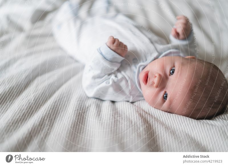 Niedliches neugeborenes Baby auf zerknittertem Bett ruhend unschuldig neugierig achtsam süß sanft Porträt heimwärts Harmonie Säugling Stoff idyllisch Fokus