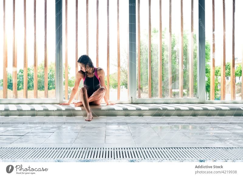 Schwimmerin im Badeanzug, die sich nach dem Training am Fenster ausruht ruhen Beine gekreuzt Sport Pause einsam professionell Körper Frau Fliesen u. Kacheln