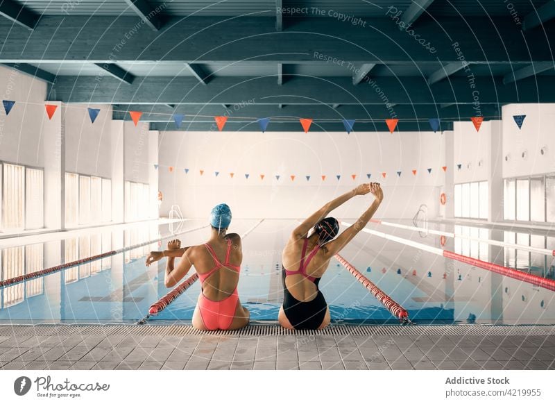 Unbekannte Schwimmer beim Aufwärmen gegen den Pool im Gebäude Sport Dehnung Training Wellness Körper Frauen Zusammensein Badebekleidung sitzen Beckenrand