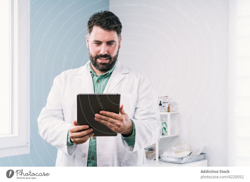 Arzt in Uniform bei der Arbeit an einem Tablet im Krankenhaus Tablette Mann professionell Internet online Klinik benutzend Apparatur Gerät Surfen zuschauend