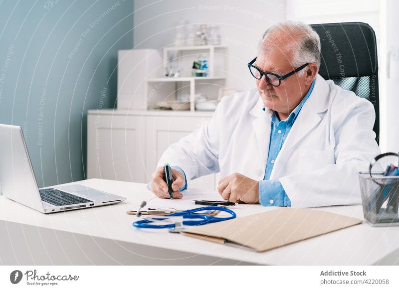 Arzt schreibt auf Papier am Tisch mit Tablet im Krankenhaus arzt zur Kenntnis nehmen Arbeit professionell Tablette ernst Uniform Mann Klinik schreiben Schot