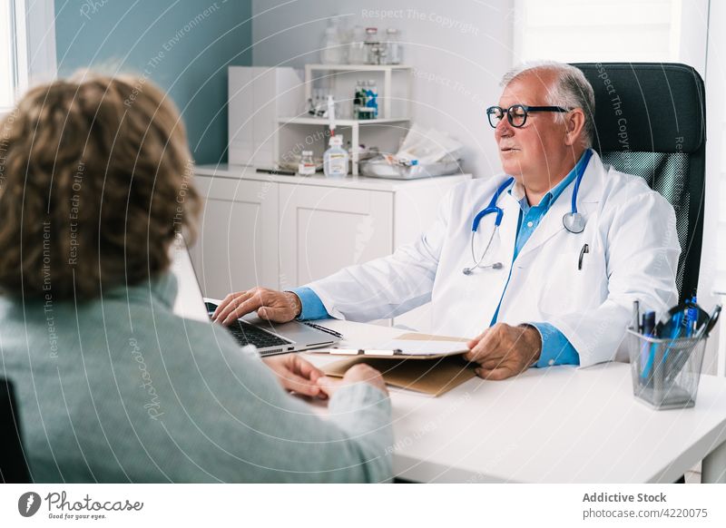 Oberarzt mit Laptop während der Beratung mit einem anonymen Patienten Arzt geduldig Tippen reden prüfen Gesundheitswesen Beruf achtsam benutzend Apparatur Mann