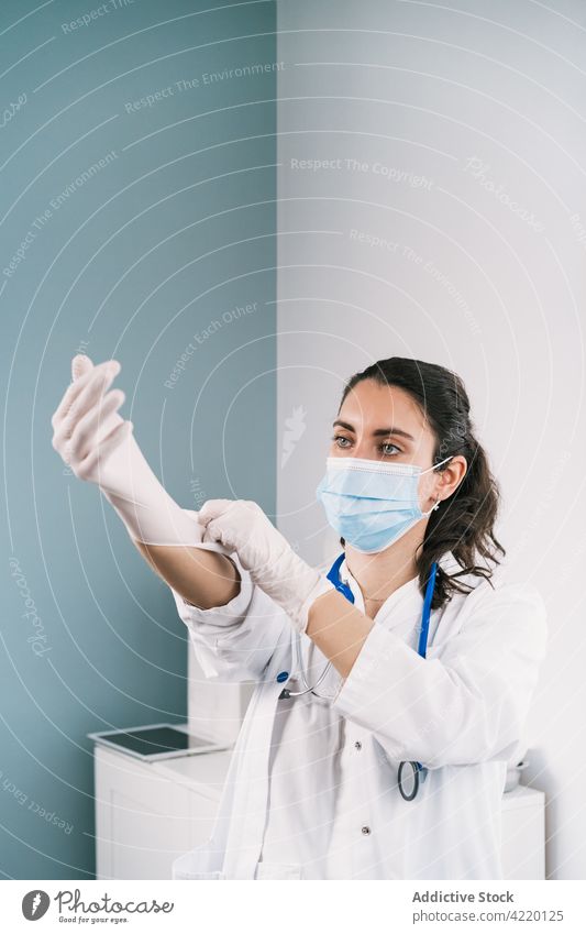 Arzt zieht bei der Arbeit in der Klinik Latexhandschuhe an arzt angezogen Handschuh professionell medizinisch Uniform behüten steril Frau Krankenhaus