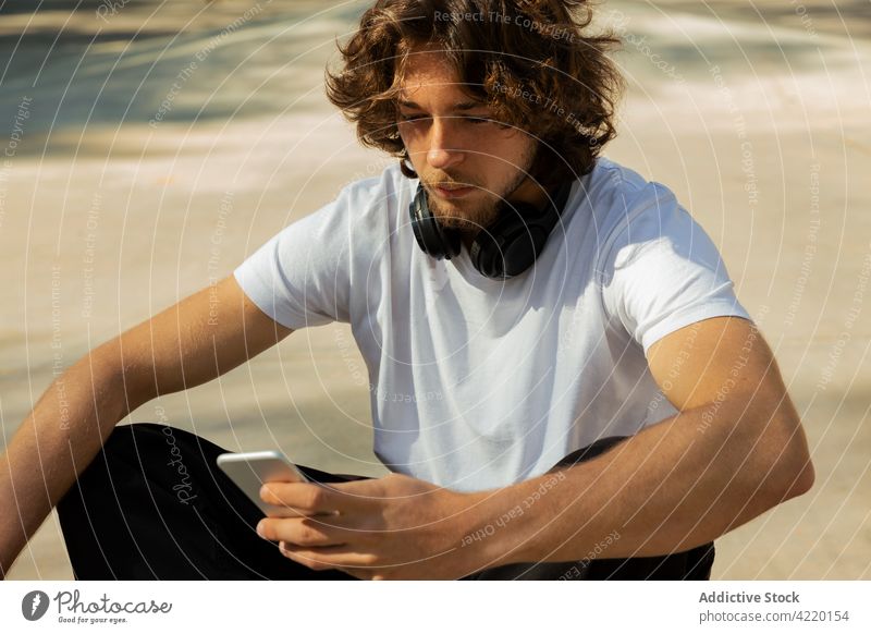 Porträt eines Skateboarders, der auf sein Handy schaut jung Mann Schlittschuhlaufen Skatepark außerhalb Kopfhörer Telefon cool horizontal Zelle Erholung