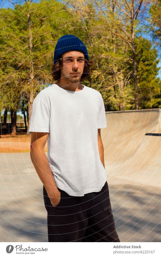 Porträt eines jungen Mannes mit Blick in die Kamera Schlittschuhlaufen blau Skateboard Beanie Hut Hose Mode Vollbart urban Großstadt T-Shirt Jugend Junge cool