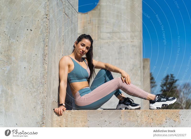 Selbstbewusste Sportlerin, die sich nach dem Training auf einer Betonfläche ausruht selbstsicher Pause Körper Kurve Sportbekleidung freundlich ruhen Porträt