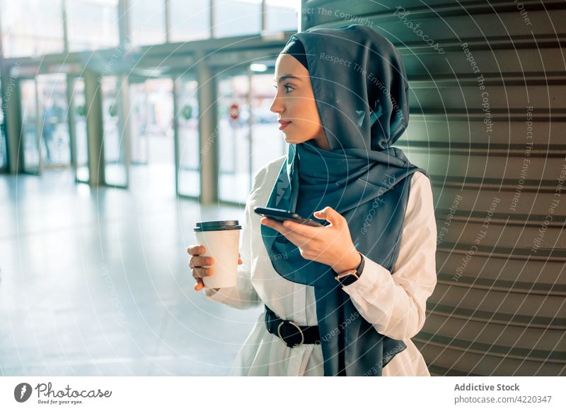 Muslimische Frau surft auf dem Bahnhof auf ihrem Smartphone Hijab warten klug Imbissbude trinken ethnisch muslimisch Funktelefon Mobile benutzend Internet