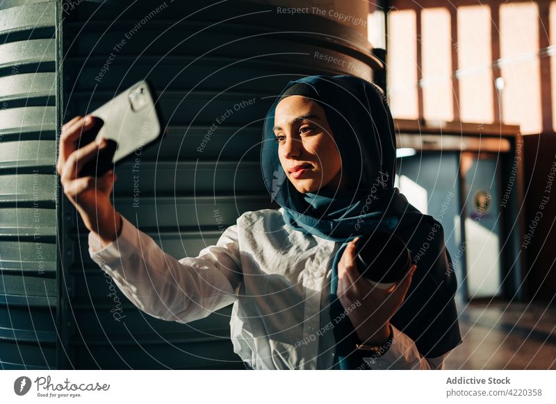 Muslimische Frau, die sich auf dem Bahnhof mit ihrem Smartphone fotografiert Selfie Hijab warten klug Selbstportrait Imbissbude trinken ethnisch muslimisch