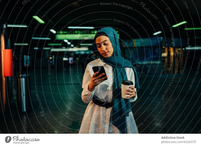 Muslimische Frau benutzt Smartphone in der U-Bahn in der Stadt Browsen unterirdisch benutzend Imbissbude Großstadt trinken Surfen Hijab ethnisch muslimisch