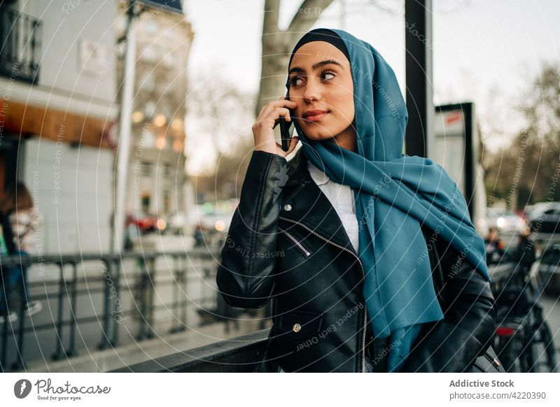Ethnische Frau im Hidschab benutzt Smartphone auf der Straße Großstadt sprechend benutzend Hijab Tradition Kopftuch Internet ethnisch muslimisch Apparatur