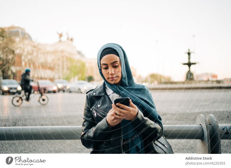 Ethnische Frau im Hidschab benutzt Smartphone auf der Straße Großstadt benutzend Browsen Hijab Tradition Kopftuch Internet ethnisch muslimisch Apparatur Mobile
