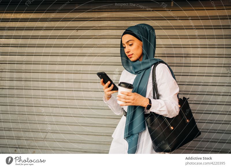 Muslimische Frau, die in der Nähe eines geschlossenen Ladens auf ihrem Smartphone surft Hijab warten klug Imbissbude trinken ethnisch muslimisch Funktelefon