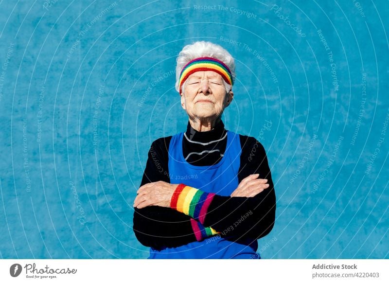 Ältere Frau in Sportkleidung stehend auf blauem Hintergrund Senior Sportlerin Sportbekleidung farbenfroh Regenbogen cool trendy älter Stil gealtert graues Haar