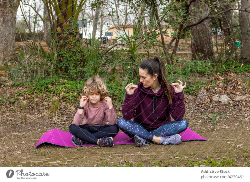 Mutter mit Sohn meditiert auf Yogamatte im Park Mama meditieren Gesunder Lebensstil Mudra Vitalität Stressabbau Beine gekreuzt Frau Lotus-Pose padmasana Asana
