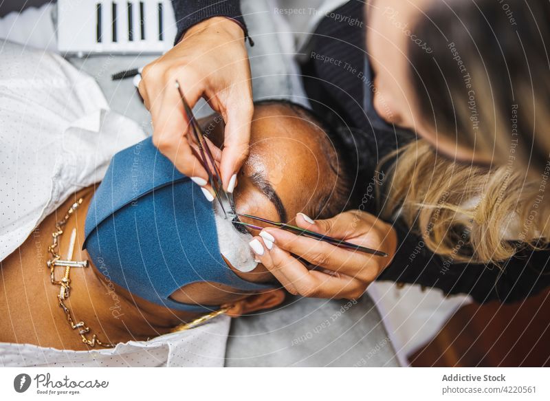 Kosmetikerin trägt Wimpern auf das Gesicht einer schwarzen Frau auf bewerben Klient Verlängerung Schönheit Kosmetologie Verfahren Frauen Salon Augen geschlossen
