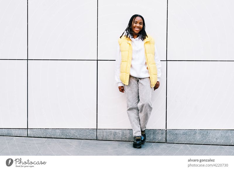 Frau lächelt, während sie sich an eine Straßenmauer lehnt. Porträt Afrikanisch Amerikaner urban schwarz im Freien Stehen Stil Großstadt Wand Zopf Frisur