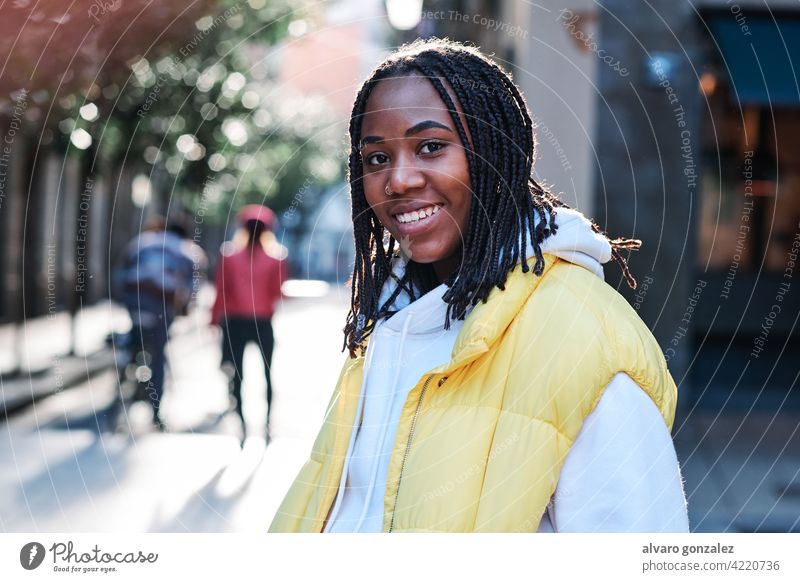 Junge Frau lächelt, während sie im Freien steht. Afrikanisch Amerikaner urban Straße schwarz Stehen Stil Großstadt Nahaufnahme Zopf Frisur Bekleidung Afro-Look