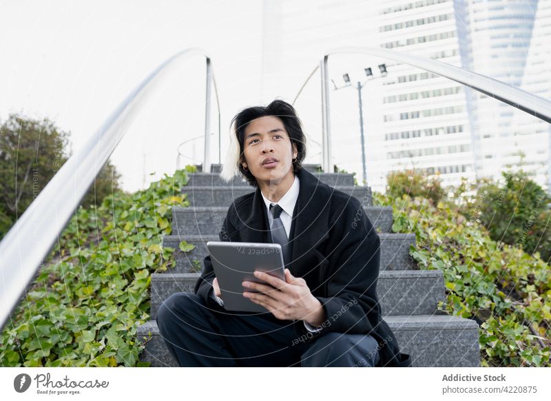 Stilvoller asiatischer Geschäftsmann mit Tablet auf einer städtischen Treppe Tablette Internet online selbständig Fokus Großstadt benutzend Apparatur Mann Gerät