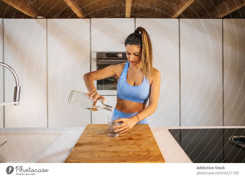 Sportler gießt in der Küche Wasser in ein Glas Athlet eingießen Flasche sportlich Vitalität frisch Frau Sportlerin Gesunder Lebensstil Wellness feminin Haus