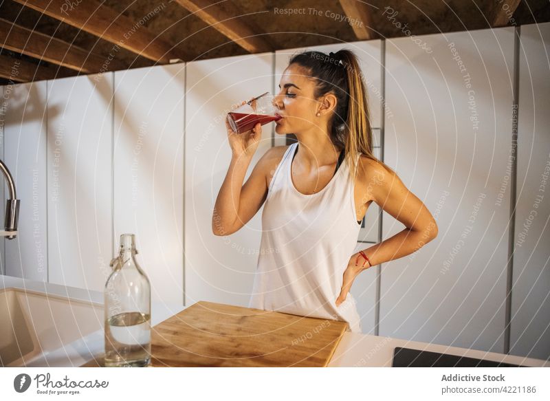 Sportlerin trinkt frischen Saft in der Küche zu Hause trinken durstig Hydrat Getränk Erfrischung Wasser Hand an der Hüfte Frau heimwärts Glas Athlet Flasche