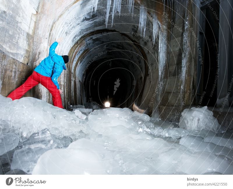 Eis und Frost, aber Licht am Ende des Tunnels. Mann blickt in einen Tunnel in den Bergen, gefrorenes Tauwasser Eiszapfen kalt Winter vereist Blick Hoffnung