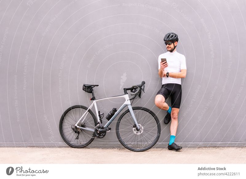 Fahrradfahrer mit Smartphone vor modernem Fahrrad auf grauem Hintergrund Radfahrer Sport selbstsicher Bein angehoben Stil Mann urban Apparatur Gerät Funktelefon