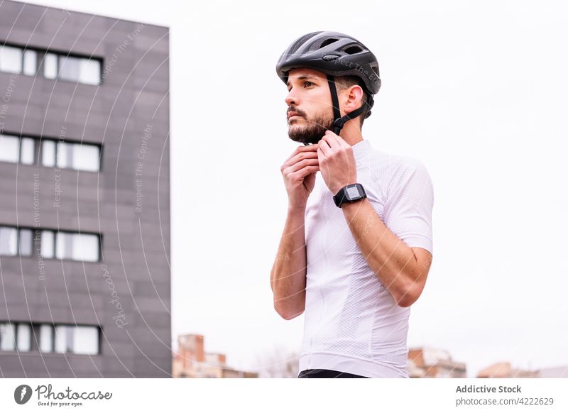 Radfahrer beim Aufsetzen des Helms auf einer Straße in der Stadt angezogen Schutzhelm Sport Fahrradfahren intelligente Uhr passen maskulin Mann Gebäude
