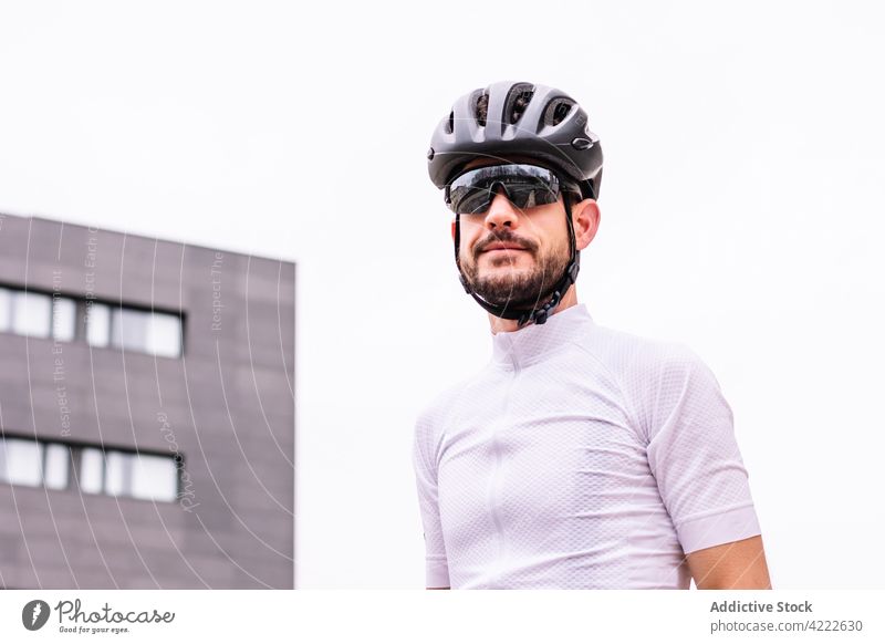 Radfahrer mit Schutzhelm und Sport-T-Shirt in der Stadt Sonnenbrille Stil professionell modern maskulin Macho Mann brutal Gebäude Sportler viril schützend Gerät