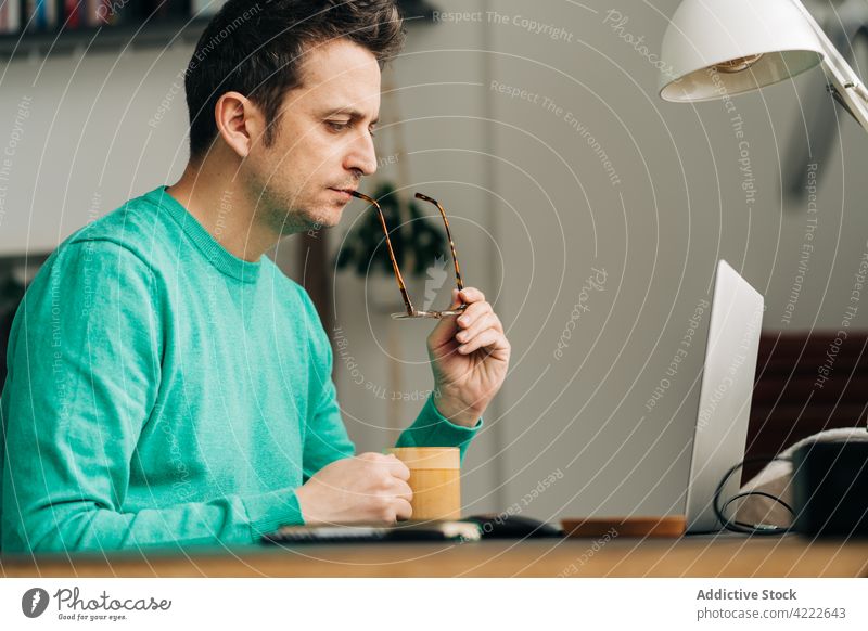 Fernangestellter mit Kaffee am Laptop zu Hause Mitarbeiter freiberuflich intelligent Arbeit Projekt Mann heimwärts benutzend Apparatur Gerät zuschauend Netbook