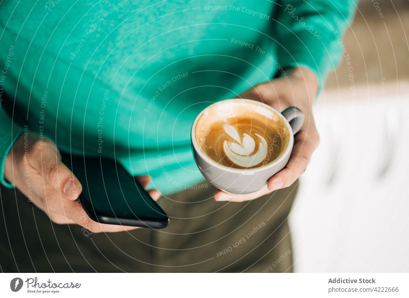Mann mit Milchkaffee, der in der Küche mit seinem Smartphone chattet plaudernd Latte Kaffee freie Zeit Internet online benutzend Apparatur Gerät Funktelefon