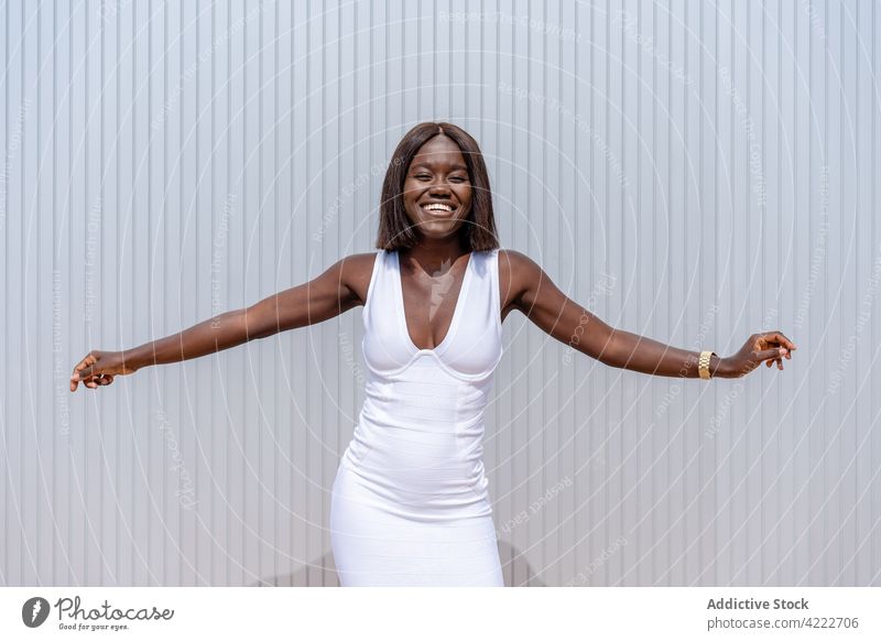 Fröhliche schwarze Frau mit ausgestreckten Armen auf dem Bürgersteig Stil Freude ausdehnen trendy Zahnfarbenes Lächeln expressiv Stimmung cool Wand Inhalt