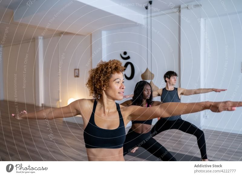 Ethnische schwarze Frau während einer Yoga-Gruppenstunde Klasse Lektion Menschen Zusammensein üben Krieger zwei Menschengruppe rassenübergreifend multiethnisch